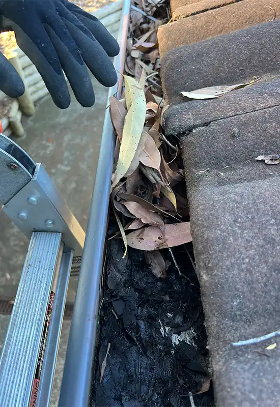 Clearing debris from very full gutters in Glenning Valley